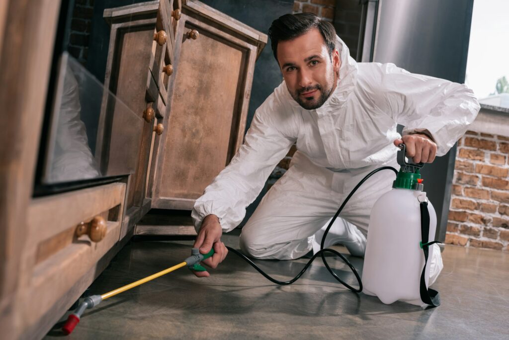 pest control worker spraying pesticides under cabinet in kitchen